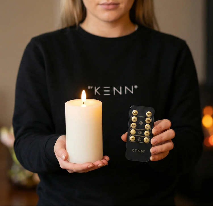 Iemand houdt een oplaadbare stompkaars vast met afstandsbediening in een woonkamer met gezellige kachel