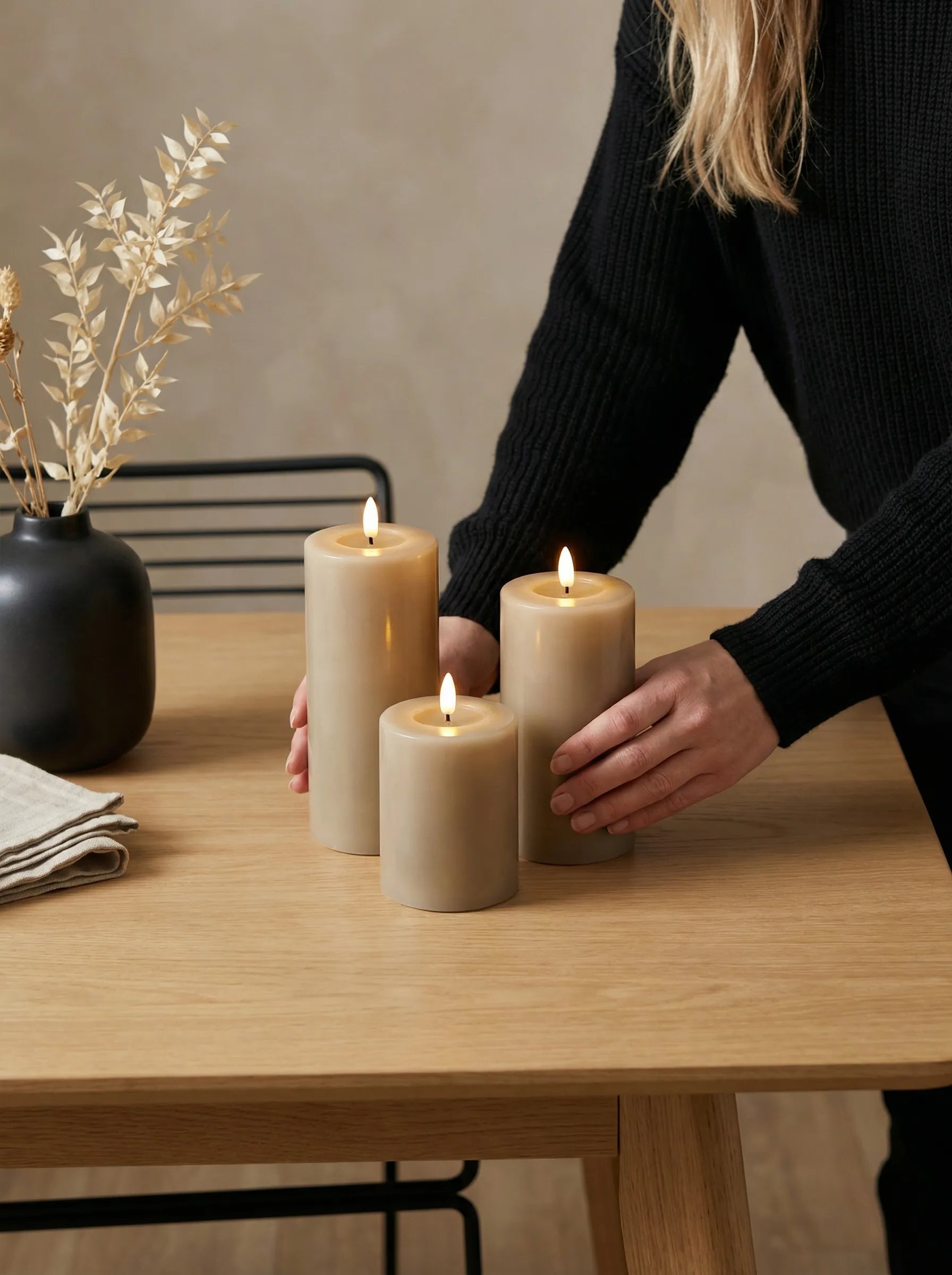 Vrouw plaatst GlowPro oplaadbare stompkaarsen op een houten tafel met zwarte vaas.